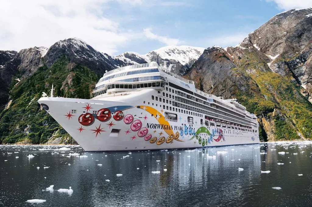 Norwegian Pearl sailing on icy water near snow capped mountains.