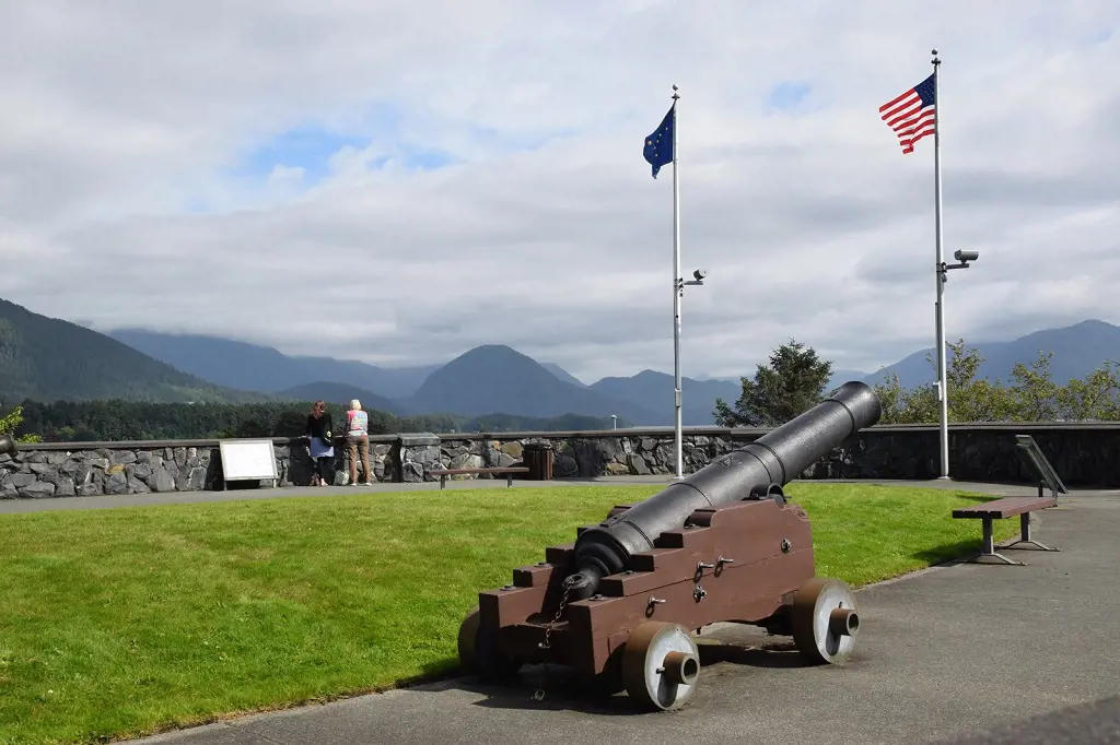 A cannon standing next to flag of Alaska state and the flag of the United States 